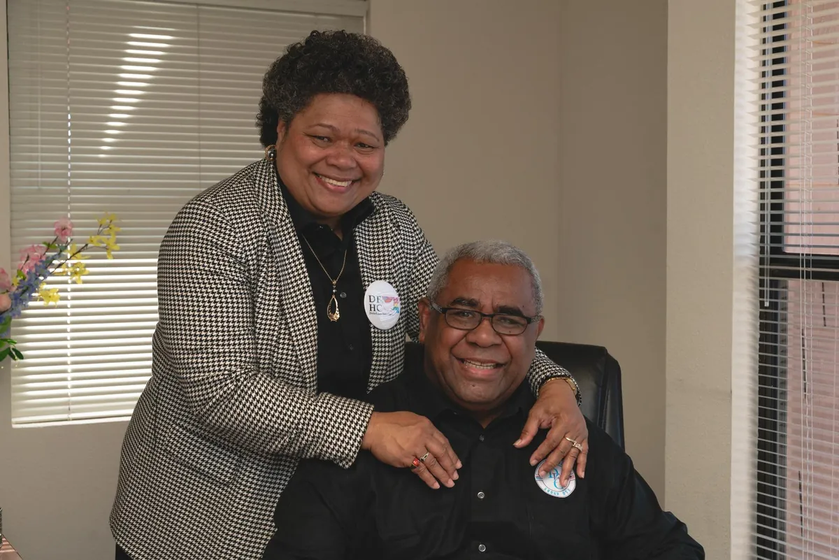 A woman standing beside a seated man, both smiling.